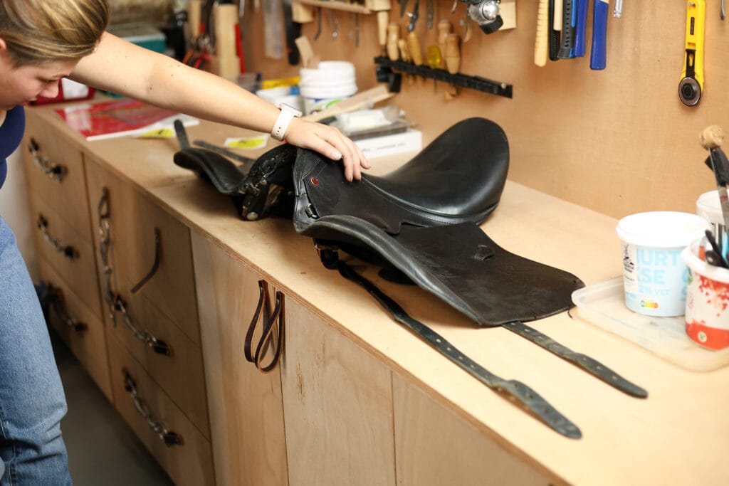 Persoon controleert de zadelboom van een zwart zadel op de werkbank in de zadelmakerij.